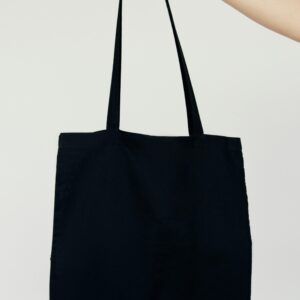 Home Minimalist image of a hand holding a blank black tote bag against a neutral background.
