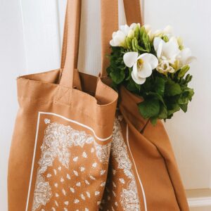 Home A stylish brown tote bag with white floral design and fresh flowers.